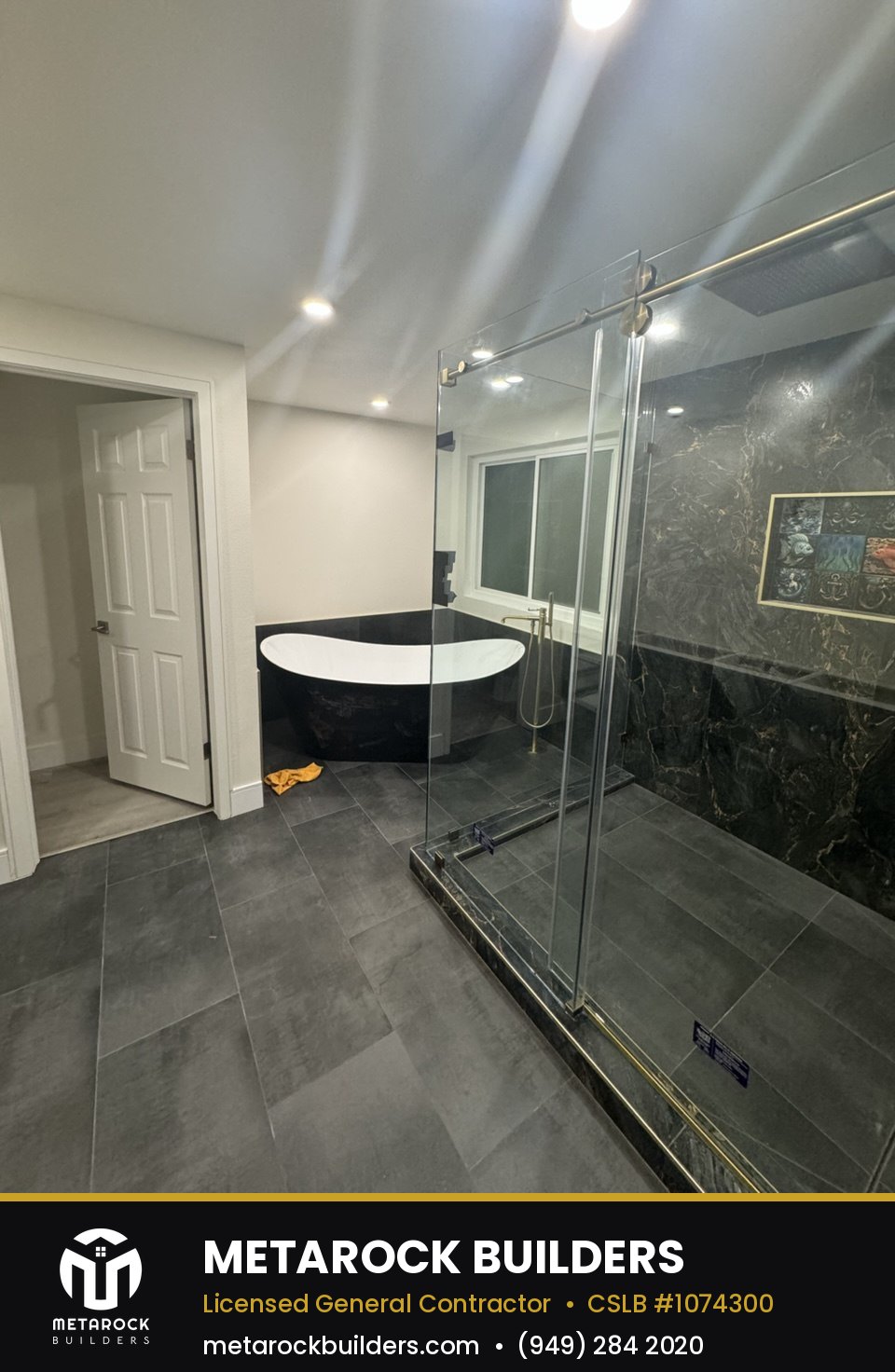 Bathroom remodel in Orange County by Sunward Builders Inc., completed after photo with dark marble-look tile, freestanding tub, and frameless glass shower with brushed brass hardware