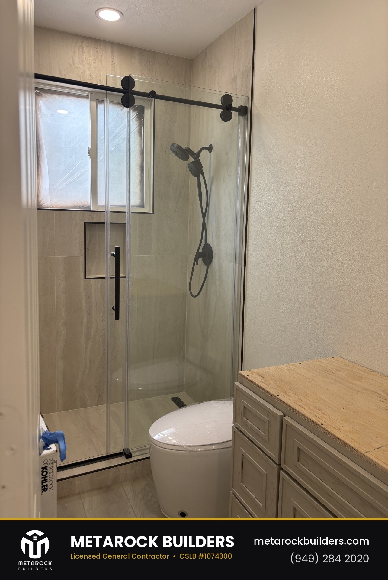 Shower remodel in Orange County by Sunward Builders Inc., completed after photo with travertine-look tile walls, frameless sliding glass door, matte black hardware, and built-in niche