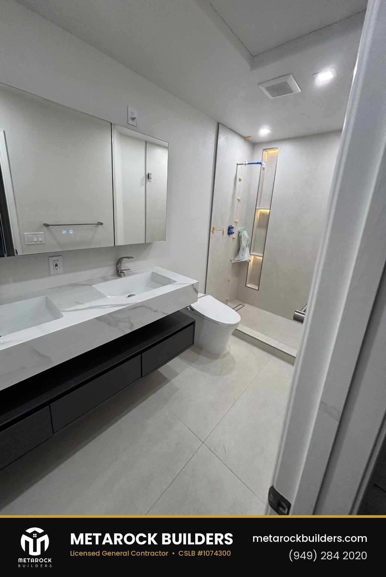 Bathroom and shower remodel in Orange County by Sunward Builders Inc., completed after photo with floating double-sink marble vanity, black cabinetry, integrated medicine cabinet, and micro-cement walk-in shower with lit niche