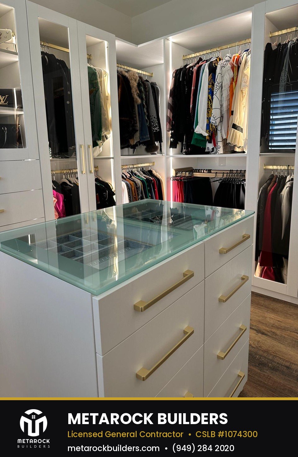 Closet remodel in Orange County by Sunward Builders Inc., completed after photo with glass-top jewelry island and illuminated hanging sections