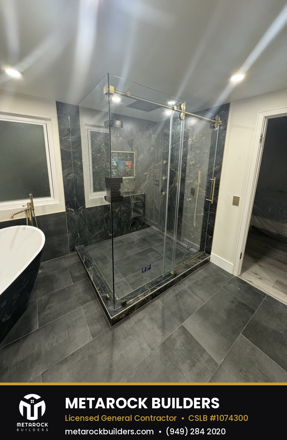 Bathroom remodel in Orange County by Sunward Builders Inc., completed after photo with book-matched black marble shower walls, brushed brass fixtures, built-in niche, and frameless glass enclosure