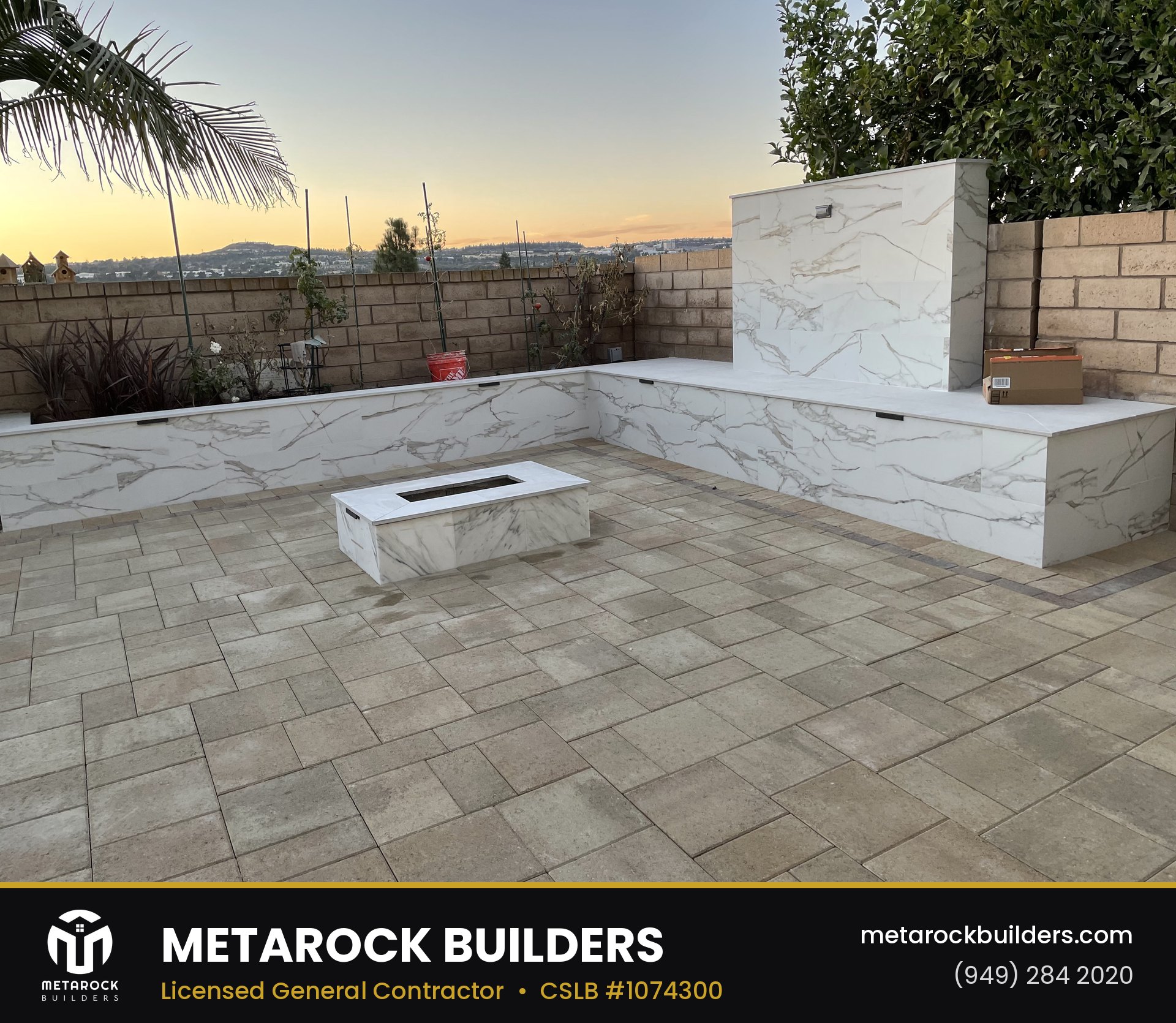 Paver patio in Orange County by Sunward Builders Inc., completed after photo with gray stone pavers, marble-clad built-in bench seating, marble fire feature, and linear gas fire pit at sunset